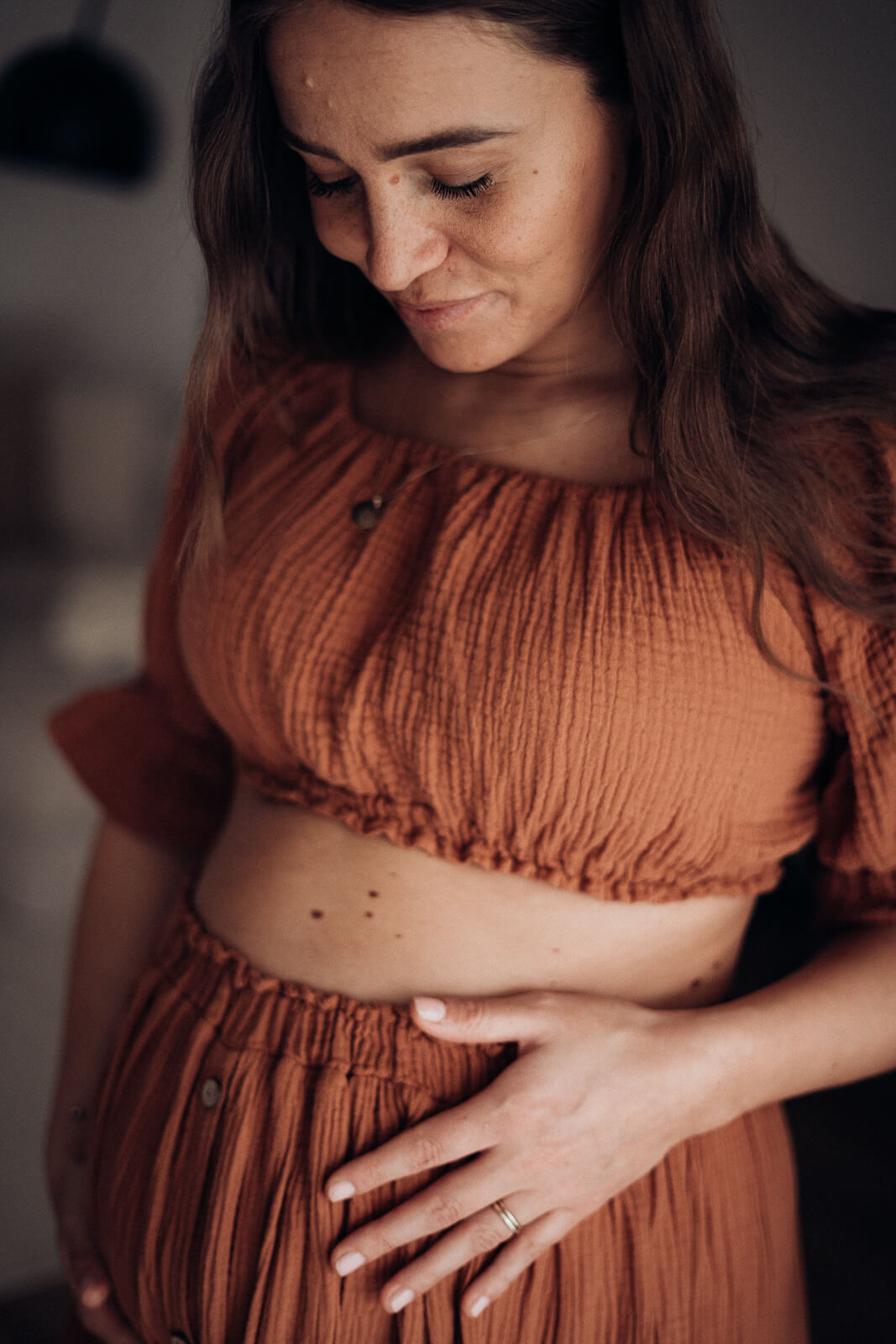 Nahaufnahme einer Schwangeren bei ihrem Babybauchshooting zuhause, mit dem Blick auf ihren Babybauch.
