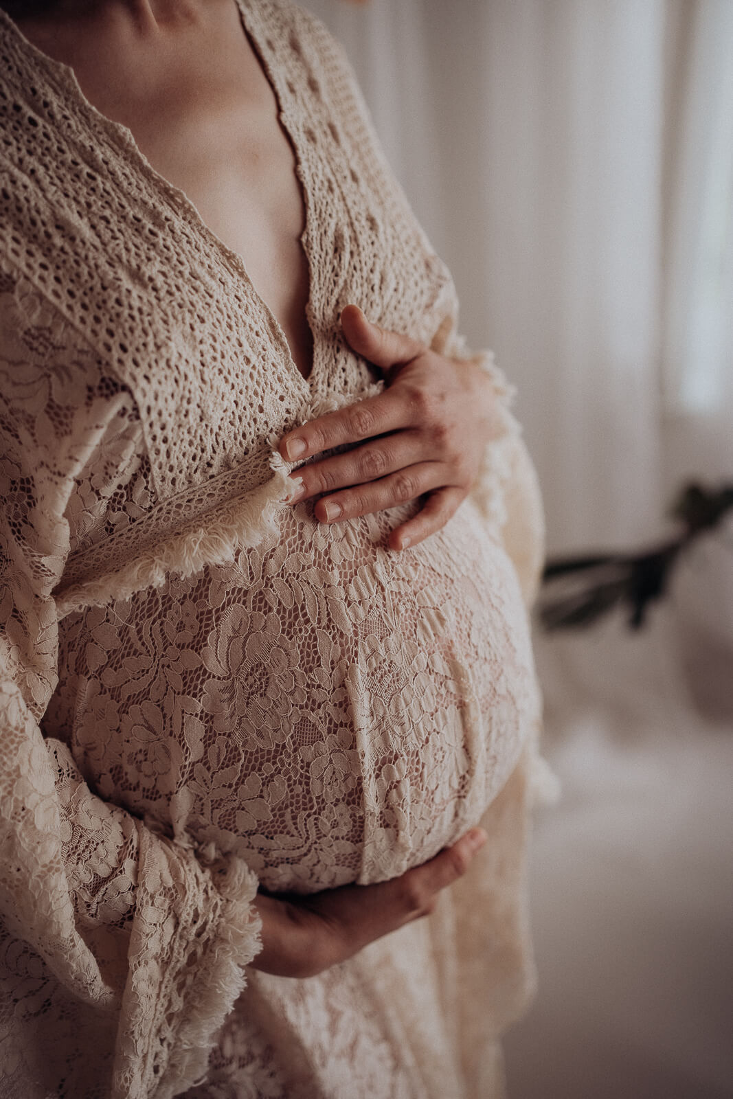Nahaufnahme bei einem Babybauchshooting bei der nur der Babybauch zu sehen ist und die Hände einer Schwangeren, die im Stehen zärtlich ihren Babybauch hält.