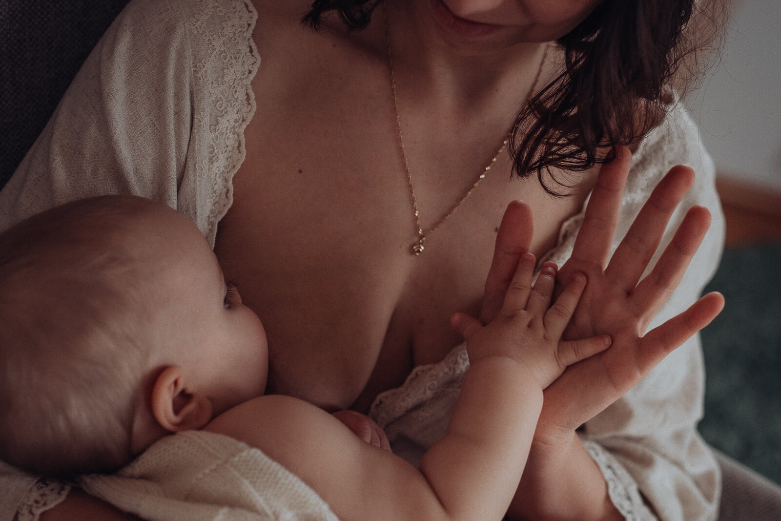 Kleine Babyhand liegt in großer Hand der Mama, während das Baby in Mamas Arm gestillt wird.