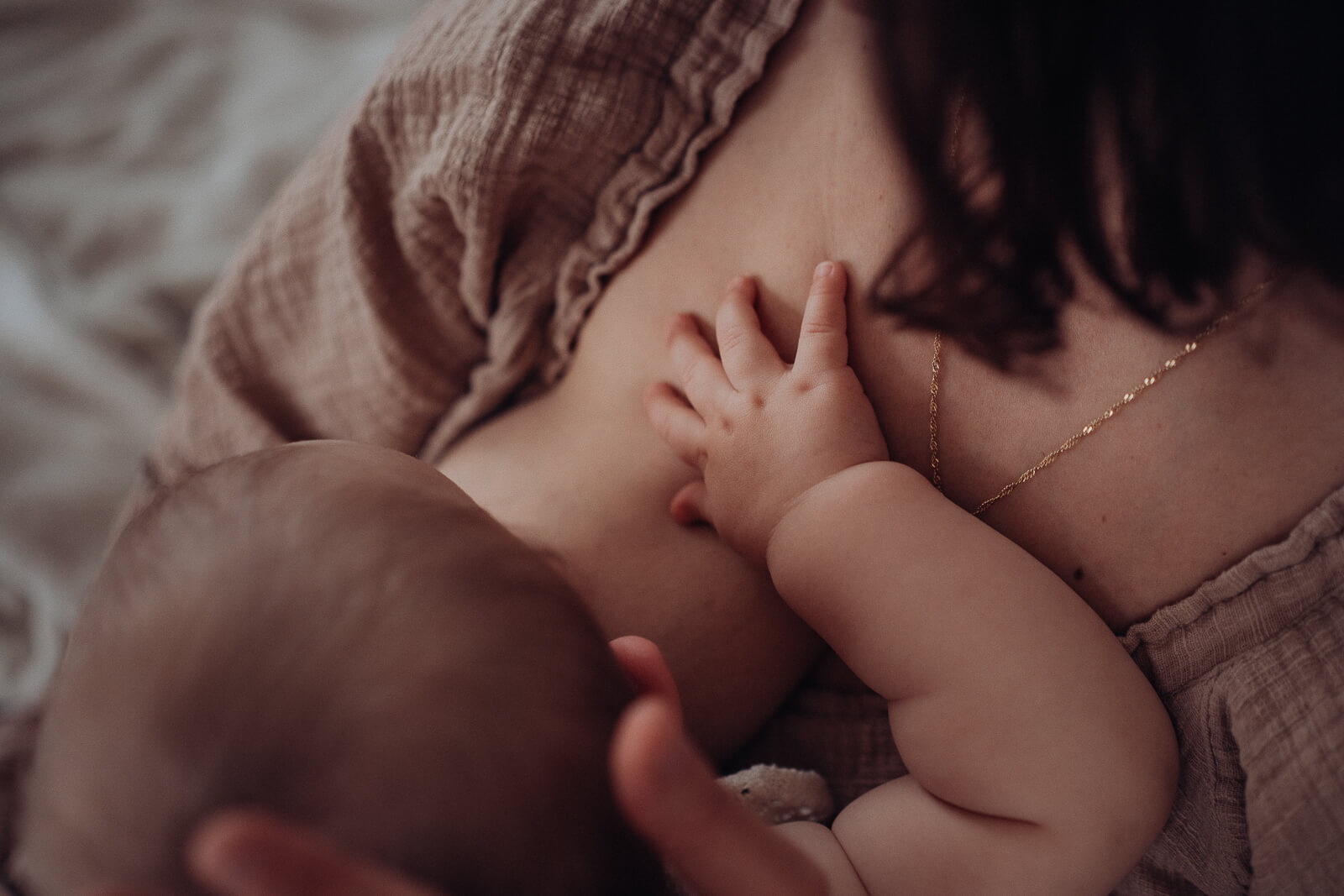 Detailaufnahme beim Stillen zwischen Mama und Baby, wie die kleine Hand des Babys auf Mamas Brust liegt.