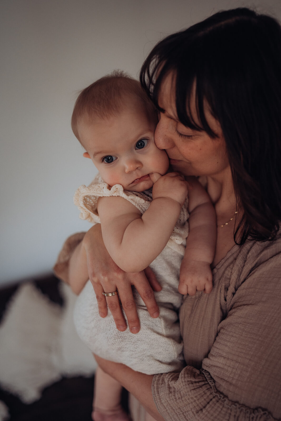 Nahaufnahme einer Mama, die im Wohnzimmer steht und ihrem Baby auf dem Arm zärtlich einen Kuss auf die Wange drückt.