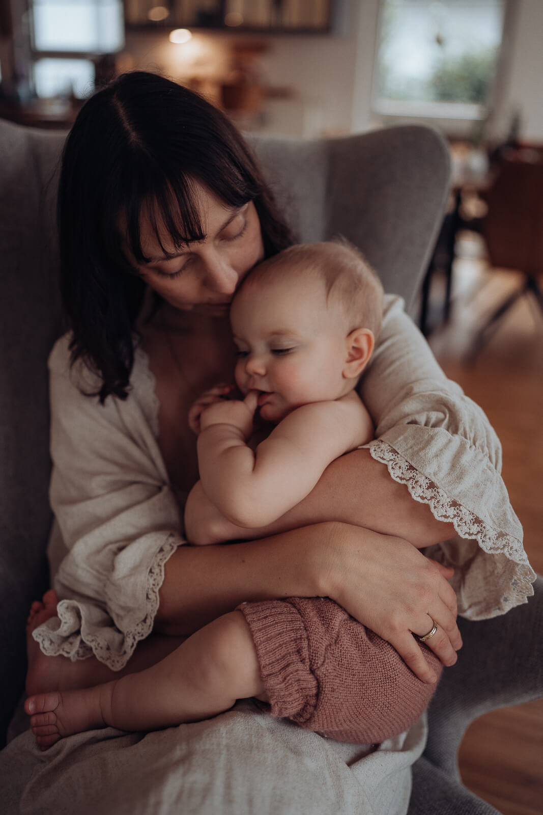 Mama sitzt im Sessel und kuschelt mit Baby im Arm