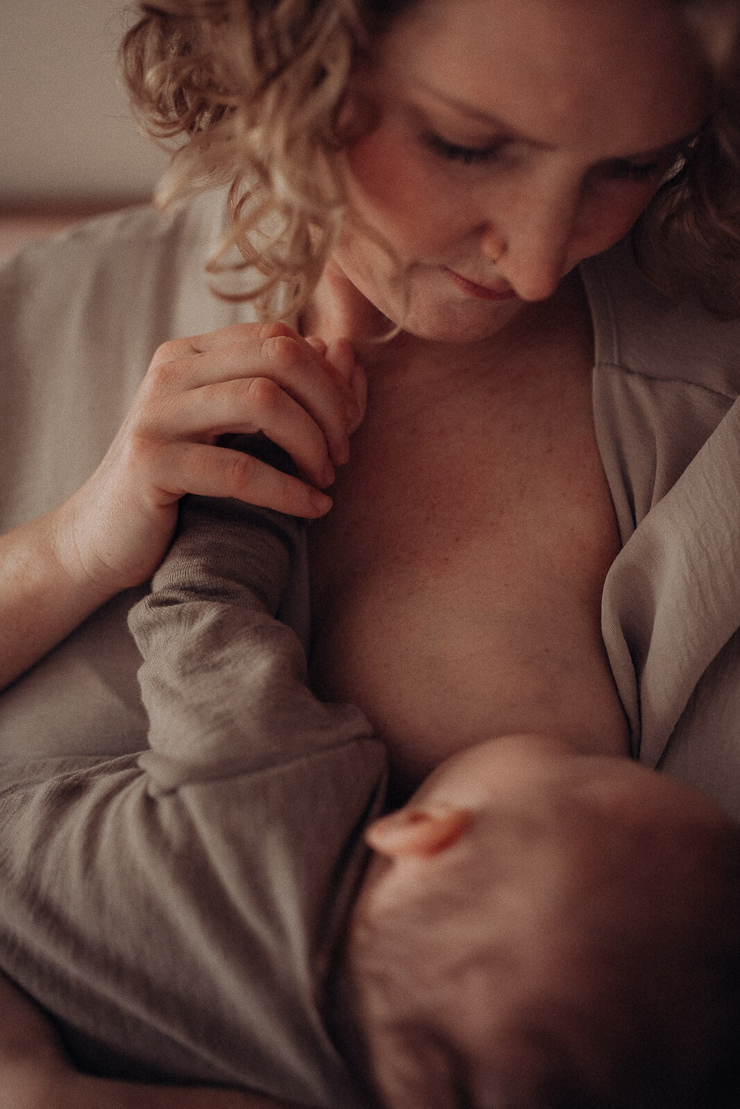 Ein Blick voller Liebe einer stillenden Mama während sie zärtlich die Hand ihres Babys hält.